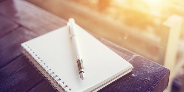 A blank notebook and pen sit on the edge of a table at sunrise.