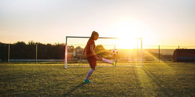 A young soccer player practices with a ball near the goal at sunset.