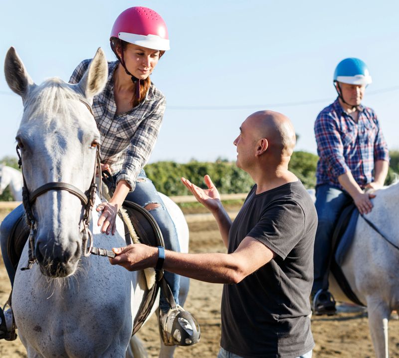 Trainer talking to female while riding horse at ranch in summer day