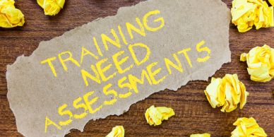 Paper with "TRAINING NEED ASSESSMENTS" and crumpled yellow papers.
