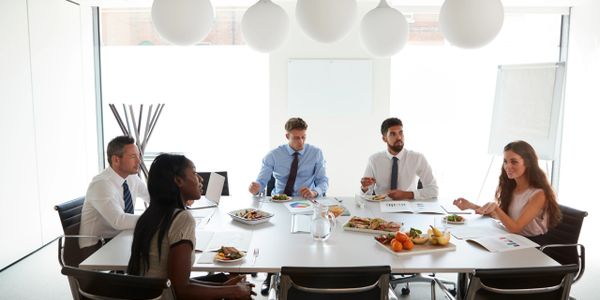 Five professionals having a meeting with food in a bright office.