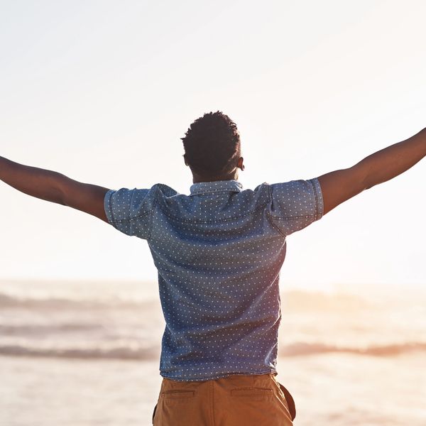 brown skinned man with arms outstretched  and looking up to the sky
blue shirt and tan chinos
