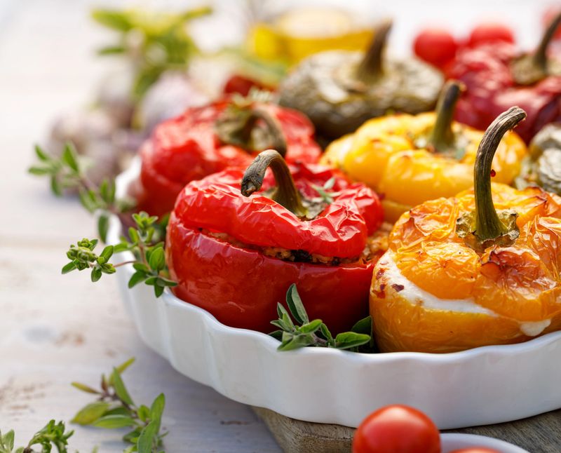 Roasted bell pepper with mushroom, rice, cheese and herbs filling in a baking dish on a white wooden table, close-up. A healthy and delicious vegetarian food.