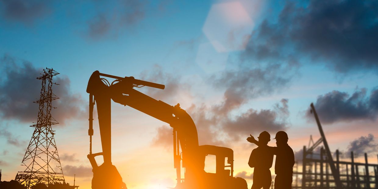Silhouettes of construction workers and machinery at sunset.