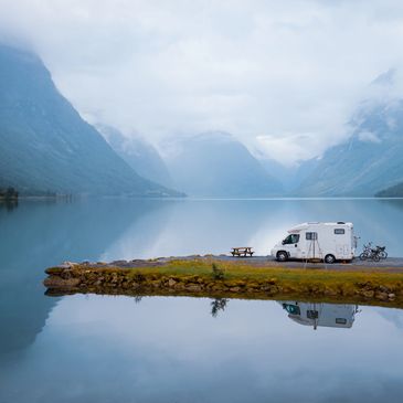 Camper van parked by a serene lake surrounded by misty mountains.