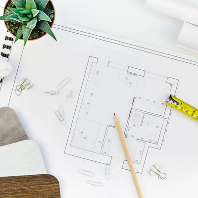 Architectural blueprint with pencil, measuring tape, and plant on white desk.