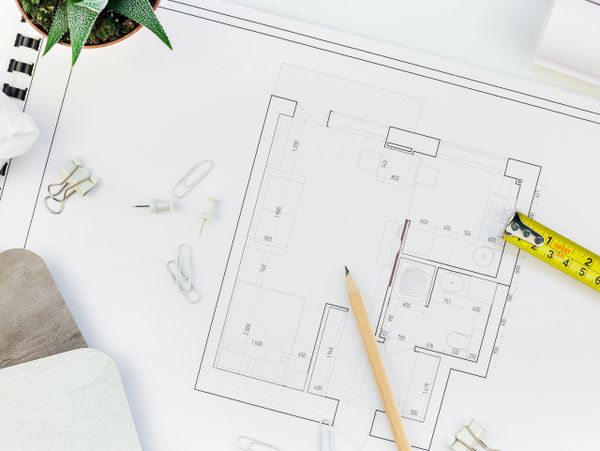 Architectural blueprint with measuring tape, pencil, and office supplies on a white desk.
