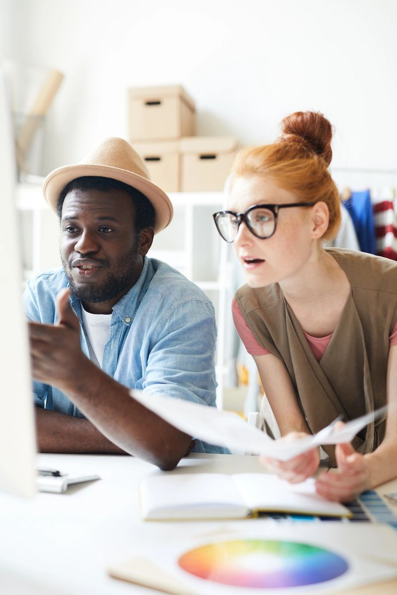 Two young creative designers looking at data on computer screen and discussing it at meeting