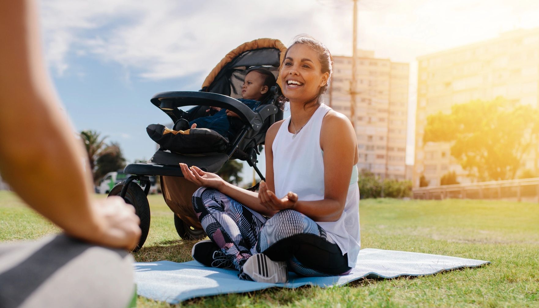 Woman sitting cross-legged on yoga mat with baby stroller behind her.