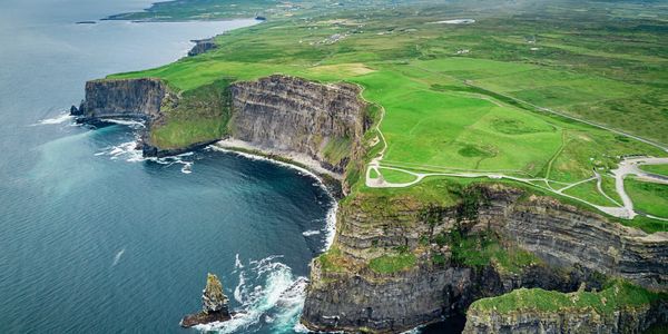 Aerial view of dramatic cliffs meeting the ocean with lush green fields above.