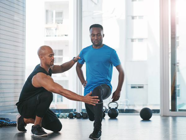 Personal trainer guiding client through a lunge exercise in a bright gym.