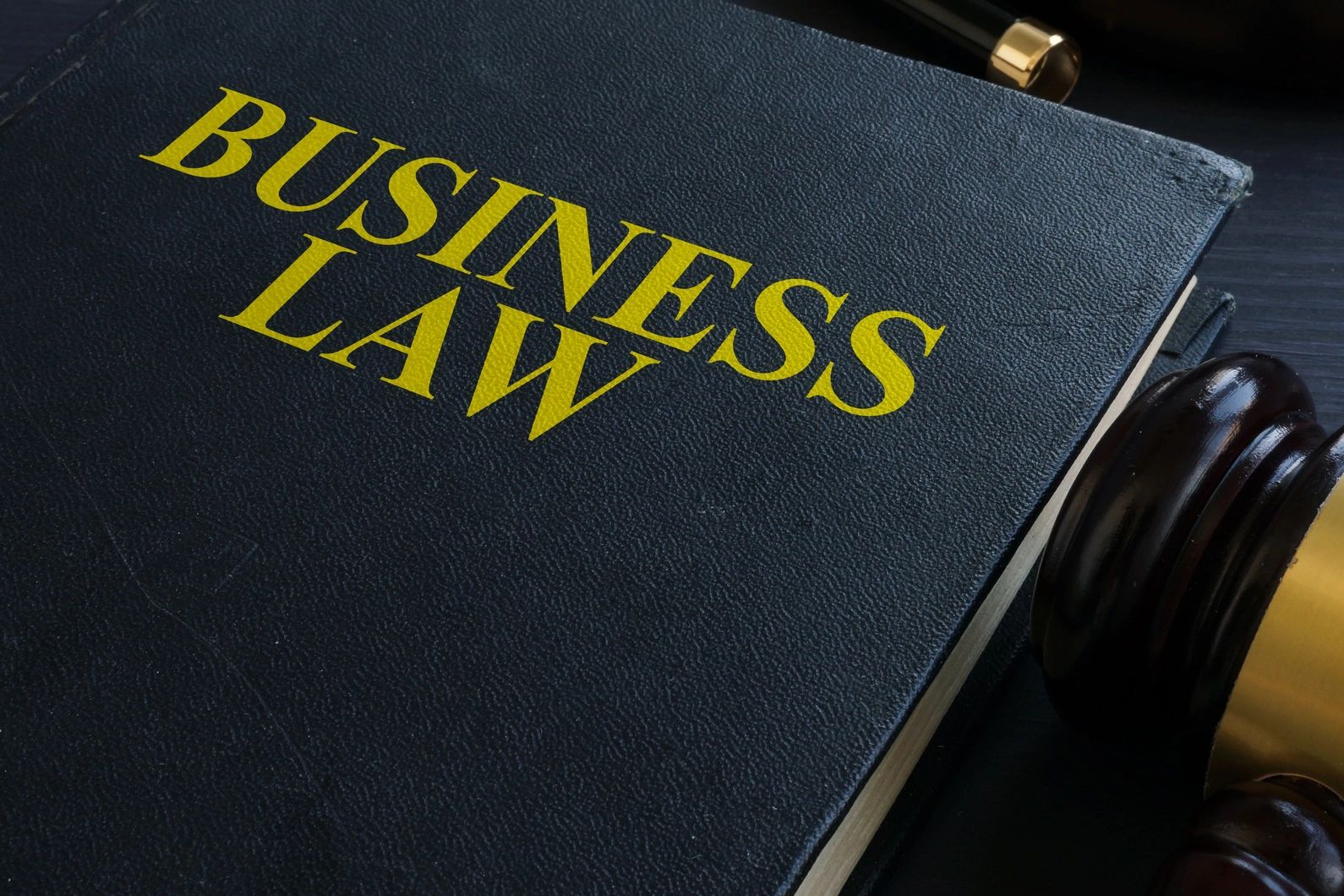 Big black book with big yellow letters that say BUSINESS LAW sitting on a desk next to a gavel.