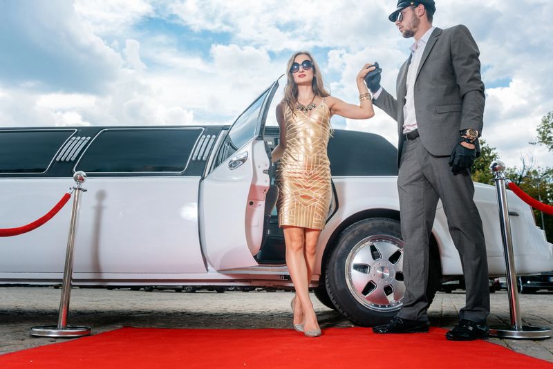 Driver helping VIP woman or star out of limo on red carpet to a reception