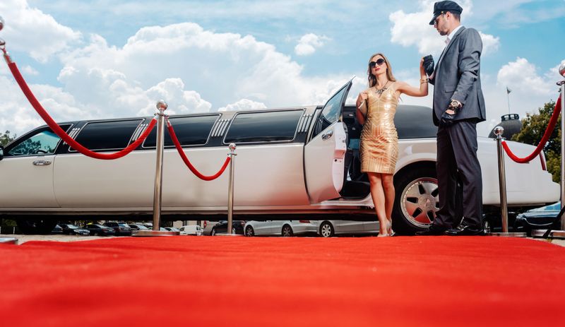 Driver helping VIP woman or star out of limo on red carpet to a reception
