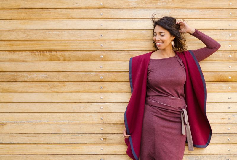 Waist up portrait of an attractive woman wearing a maroon dress and shawl standing against a wooden plank background