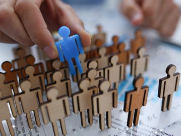 A hand selects a blue figure from a group of wooden figures.