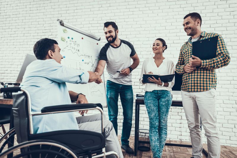 Young Workers Have Discussion in Modern Office. Brainstorm at Work. Smiling Woman. Man on Wheelchair. Smiling Manager. Teamwork in Office. Plan Presentation. Communication with Colleagues.