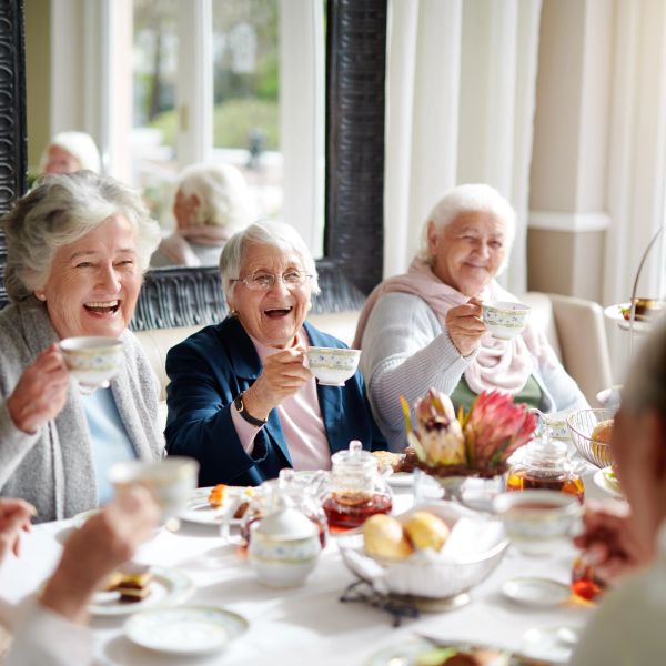 Elderly friends joyfully sharing tea and laughter at a cozy gathering.