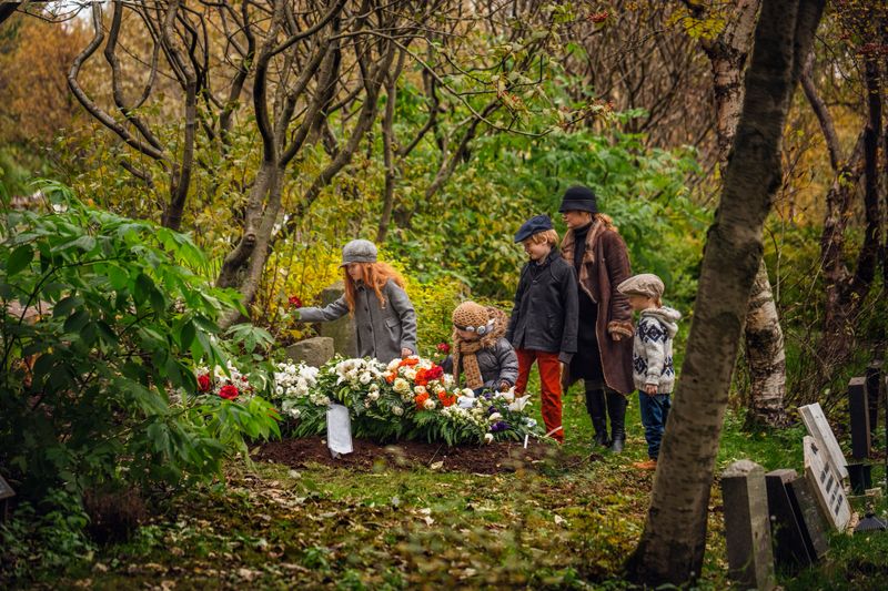 Mother and children visiting grave of deceased loved one. Family is at cemetery in forest. They are in winter wear.