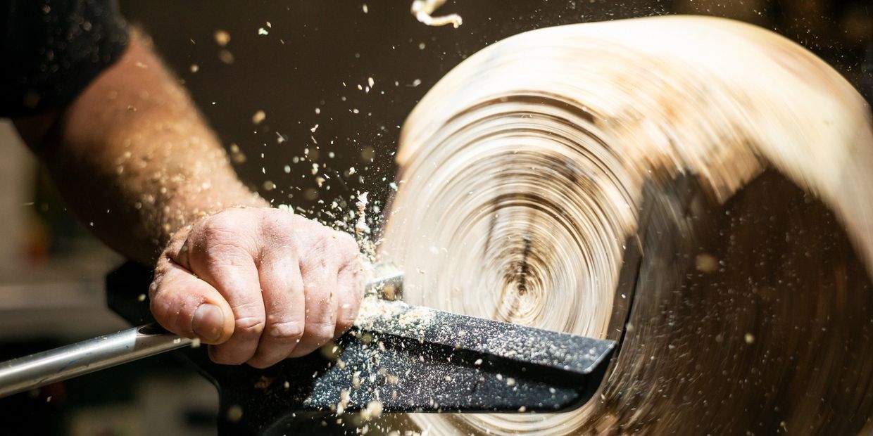 Close-up of hand shaping spinning wood on a lathe with wood shavings flying.