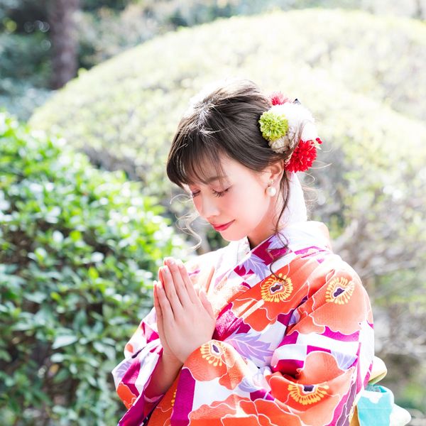 Woman in colorful kimono praying solemnly in a garden.