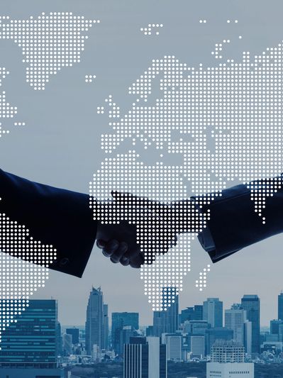 Business handshake overlaid with a dotted world map and city skyline.