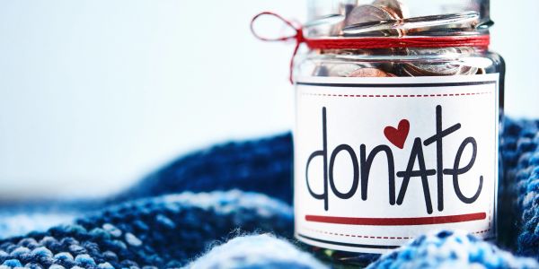 A donation jar filled with coins on a blue knitted cloth.