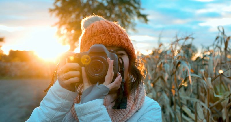 Beautiful Young Woman Taking picture with Digital Camera at Sunset close tu a Corn Field.
