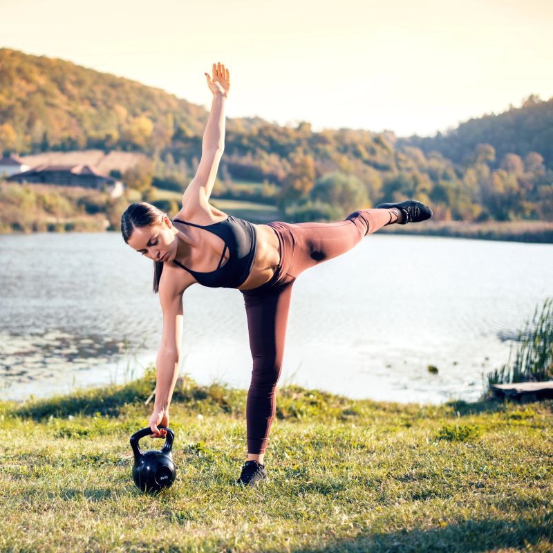 Strong young woman exercising with kettlebell next to the lake