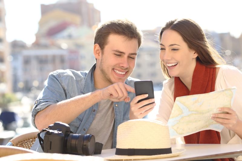 Couple of happy tourists comparing online guide in a smart phone and a paper map on vacation