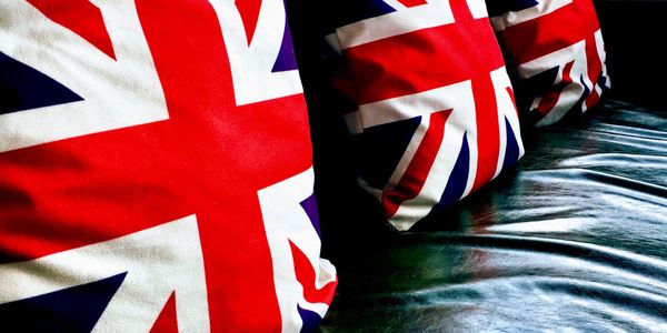 Three Union Jack pillows on a black leather couch.