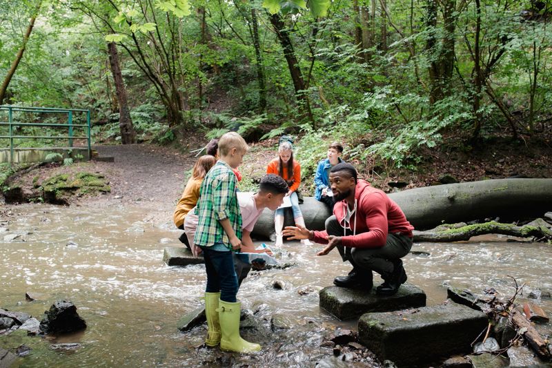 Group of school children on a field trip. They are standing in a river looking for wildlife while listening to their teacher.