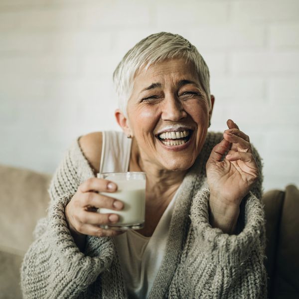 Joyful elderly woman enjoying a glass of milk with a milk mustache.