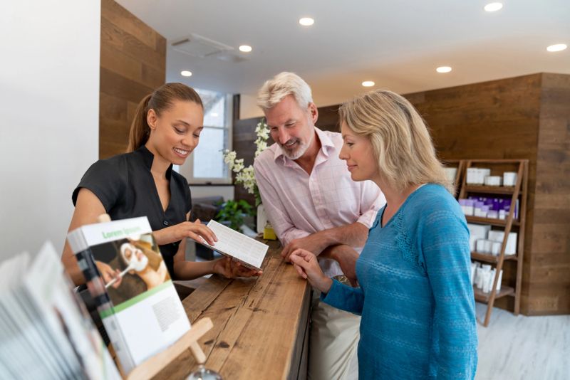 Portrait of two happy clients talking to the manager at the spa and looking at the brochure over the main counter - beauty concepts. **DESIGN ON BROCHURE IS OURS**