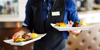 A waiter carrying two plates of gourmet food in a restaurant.