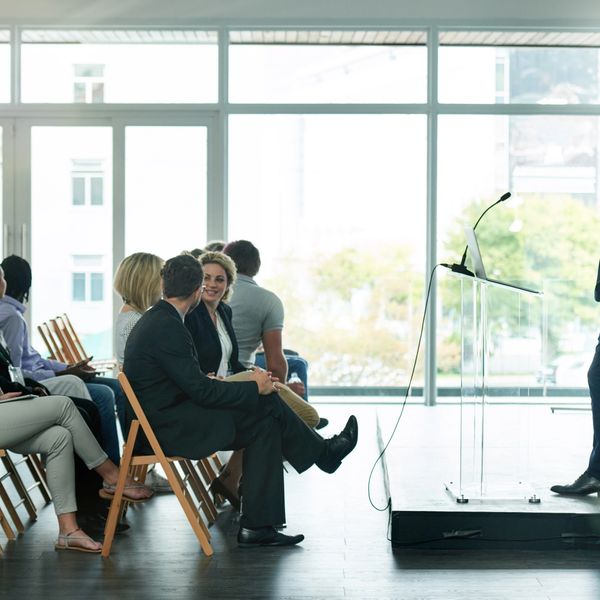 Business presentation with attendees seated and a speaker at the podium.