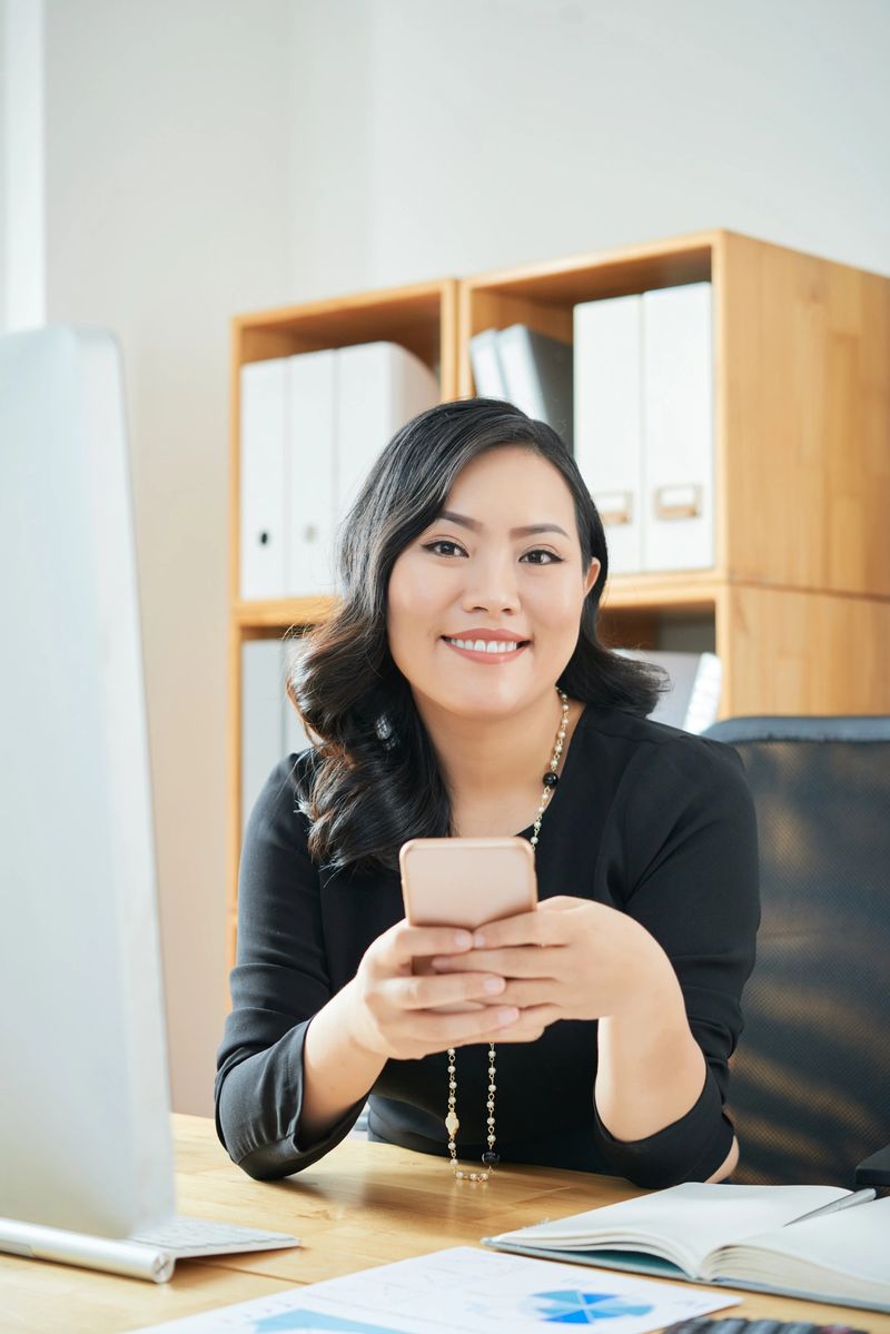 Portrait of happy young female entrepreneur with smartphone sitting at office table
