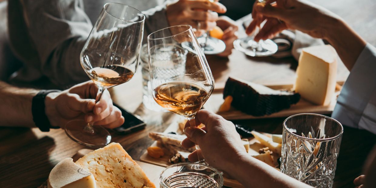 People toasting with wine over cheese plates.
