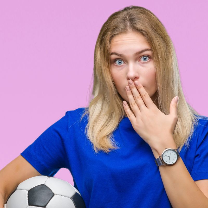 Young caucasian woman holding soccer ball over isolated background cover mouth with hand shocked with shame for mistake, expression of fear, scared in silence, secret concept