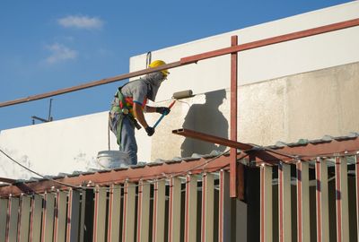 A construction worker painting a building wall with a roller.