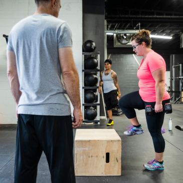 Woman exercising with weights under trainer's supervision.