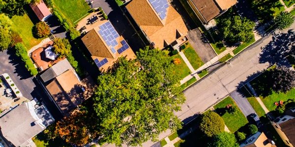 Aerial view of suburban houses with solar panels on roofs and green lawns.