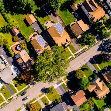Aerial view of suburban houses with solar panels on roofs and green lawns.