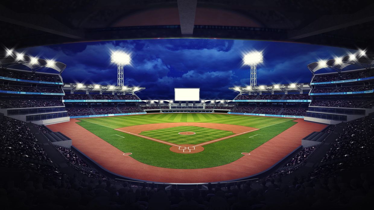 A brightly lit baseball stadium at night with a large crowd and a blank scoreboard.