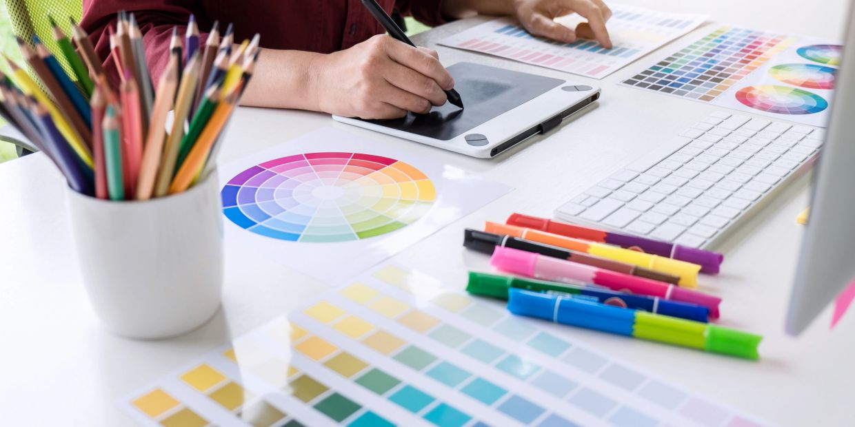 Person using tablet with color samples and drawing tools on desk.