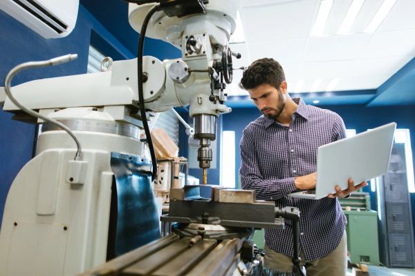 Man using laptop near milling machine.