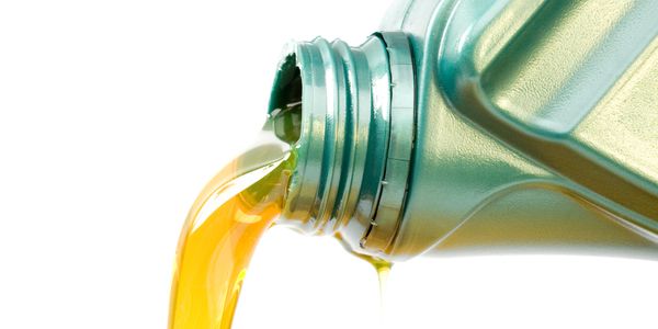 Golden engine oil pouring from a green plastic container.