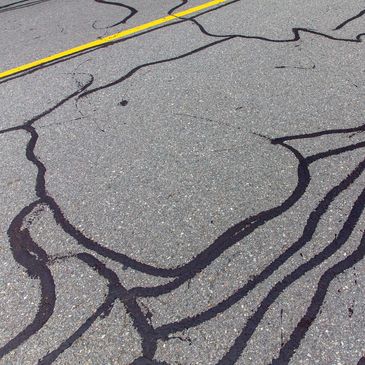 Close-up of road cracks sealed with black tar near a yellow line.