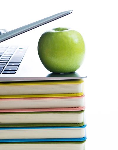 Green apple on a stack of colorful books with a laptop partially open.
