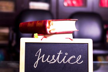 Stack of law books above a chalkboard with the word 'Justice'.